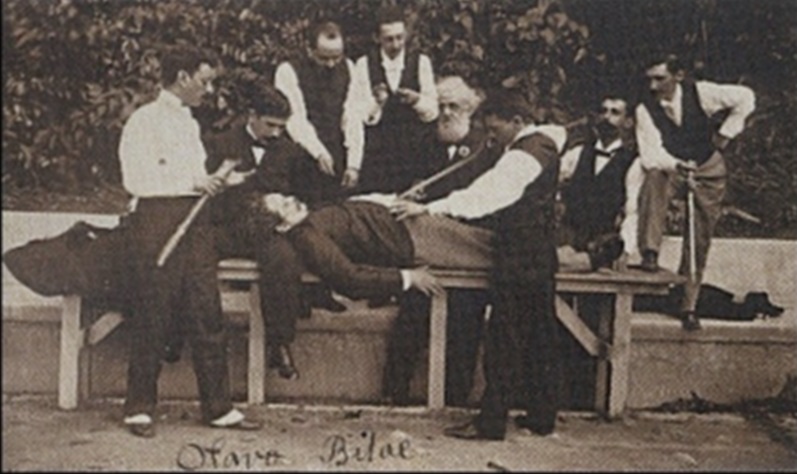 Fotografia originalmente pertencente a Olavo Bilac, com sua assinatura, em que intelectuais que participaram da fundação da Academia Brasileira de Letras encenam a "Lição de Anatomia", quadro do pintor holandês, Rembrandt. Da esquerda para a direita: Olavo Bilac, Leôncio Correia, Henrique Holanda, Pedro Rabelo, o doutor Pederneiras, Álvaro de Azevedo Sobrinho e Plácido Júnior. O autopsiado é Artur Azevedo, sendo o legista, que o opera com o sabre emprestado pelo oficial da ronda, Coelho Neto, 1900 / Wikipedia